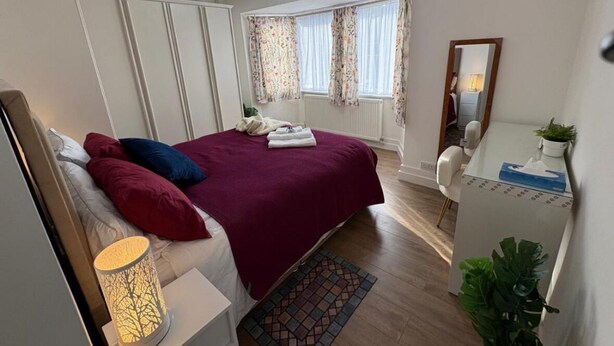 A bedroom with a bed, bedside lamp, dresser, and a window with curtains. - Modern 3BR Home with Free Parking | Sleeps 6 | Family & Business Friendly (Bracknell)