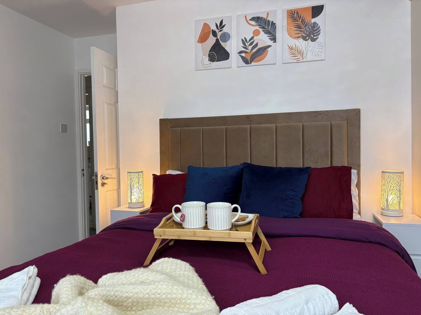 Ein Schlafzimmer mit einem Bett, Kissen, einem Tablett mit Tassen und Wandbildern.