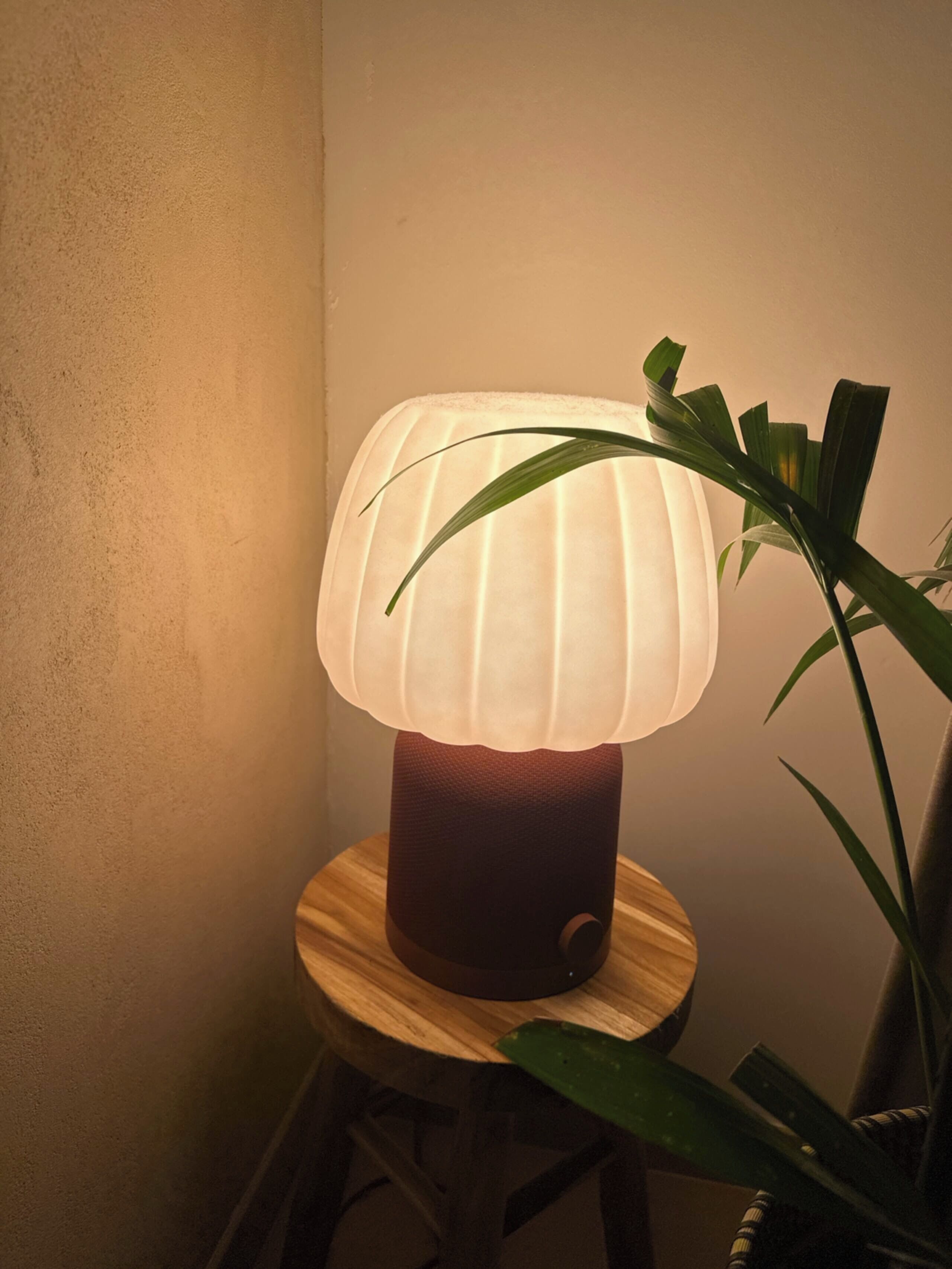 Une lampe dont le pied est strié, posée sur un tabouret en bois.