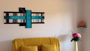 Ein Wohnzimmer mit gelbem Sofa, einer Wanddekoration, einer hängenden Papierlaterne und einer Vase mit Blumen.