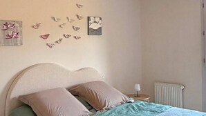 Ein Schlafzimmer mit einem Bett, Kissen, einem Nachttisch mit Lampe, einer Heizung und Wanddekorationen, darunter Schmetterlinge und eine Blume.