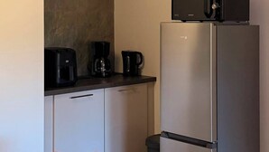 Eine kleine Küche mit Kühlschrank, Kaffeemaschine und Mikrowelle auf der Arbeitsfläche.