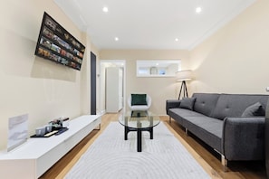 A modern living room with a flat-screen TV, a sofa, a glass coffee table, and a lamp. - Luxury one bedroom apartment sleeps up to 4 people (London)