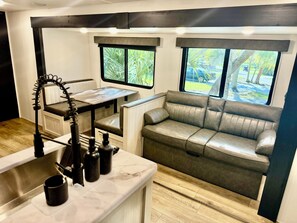 A compact kitchenette with a sink, a small table, and a seating area with a sofa and a bench. - 2-bedroom RV in Crystal River (Crystal River)