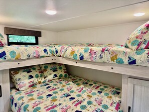 A bunk bed with a colorful quilt, a television above the top bunk, and a window with a view of greenery. - 2-bedroom RV in Crystal River (Crystal River)