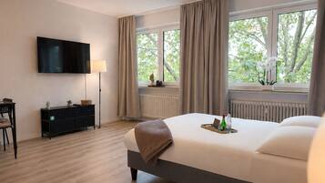 A hotel room with a bed, a TV, a desk, and a window with curtains.