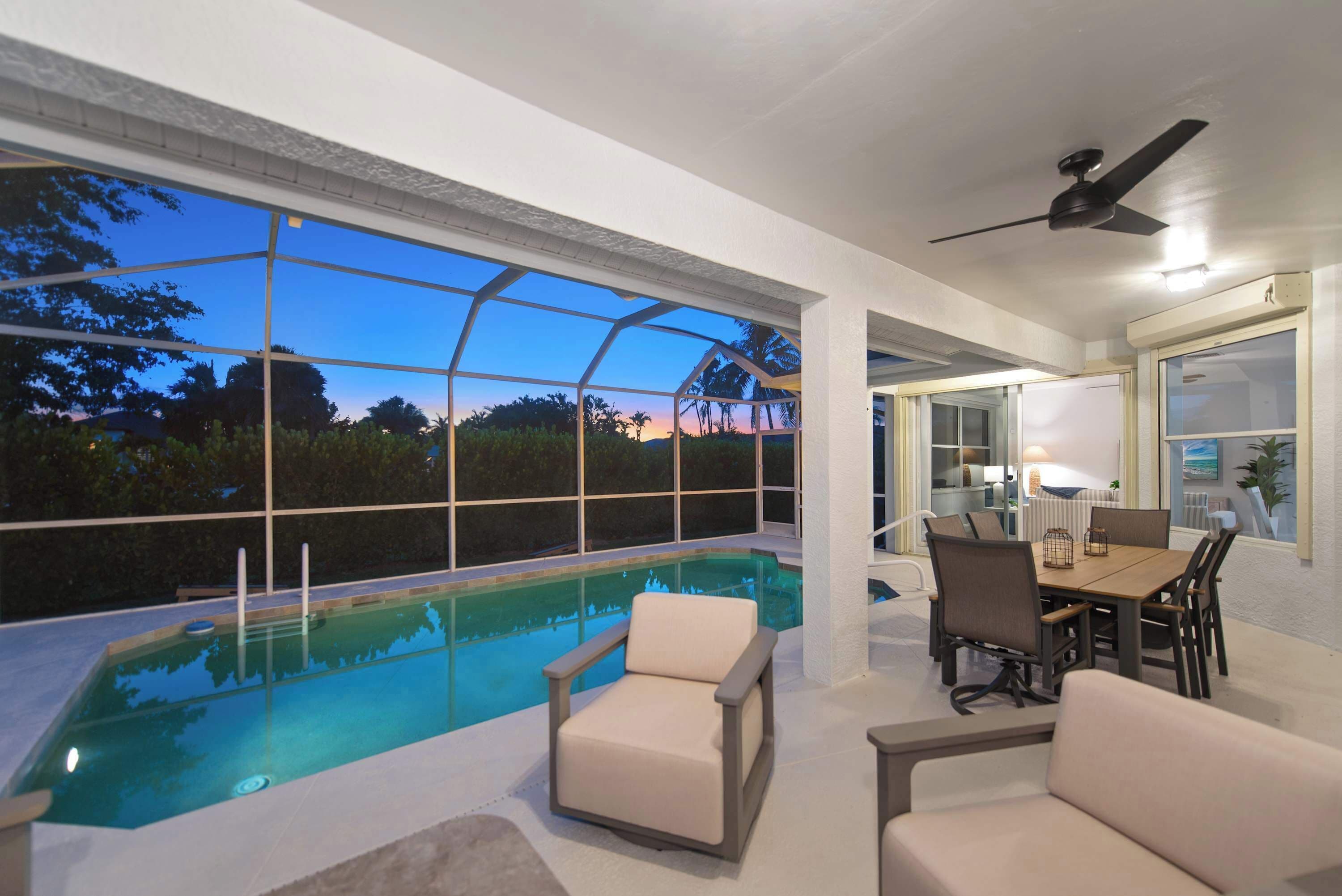 Une piscine intérieure moderne dotée d’un toit en verre, entourée d’espaces de détente et d’un coin repas.
