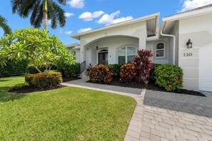 A two-story house with a well-maintained lawn, a driveway, and a variety of colorful plants. - Palm Island Retreat | Private Pool | Bikes (Marco Island)