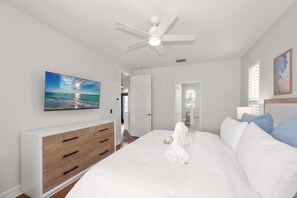 Ein Schlafzimmer mit einem Bett, einem Deckenventilator, einem Schminktisch, einem Gemälde und einem Fenster mit Jalousien.