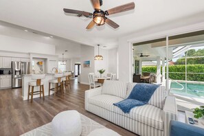 A spacious living area with a ceiling fan, a poolside seating area, and a kitchen with modern appliances. - Palm Island Retreat | Private Pool | Bikes (Marco Island)