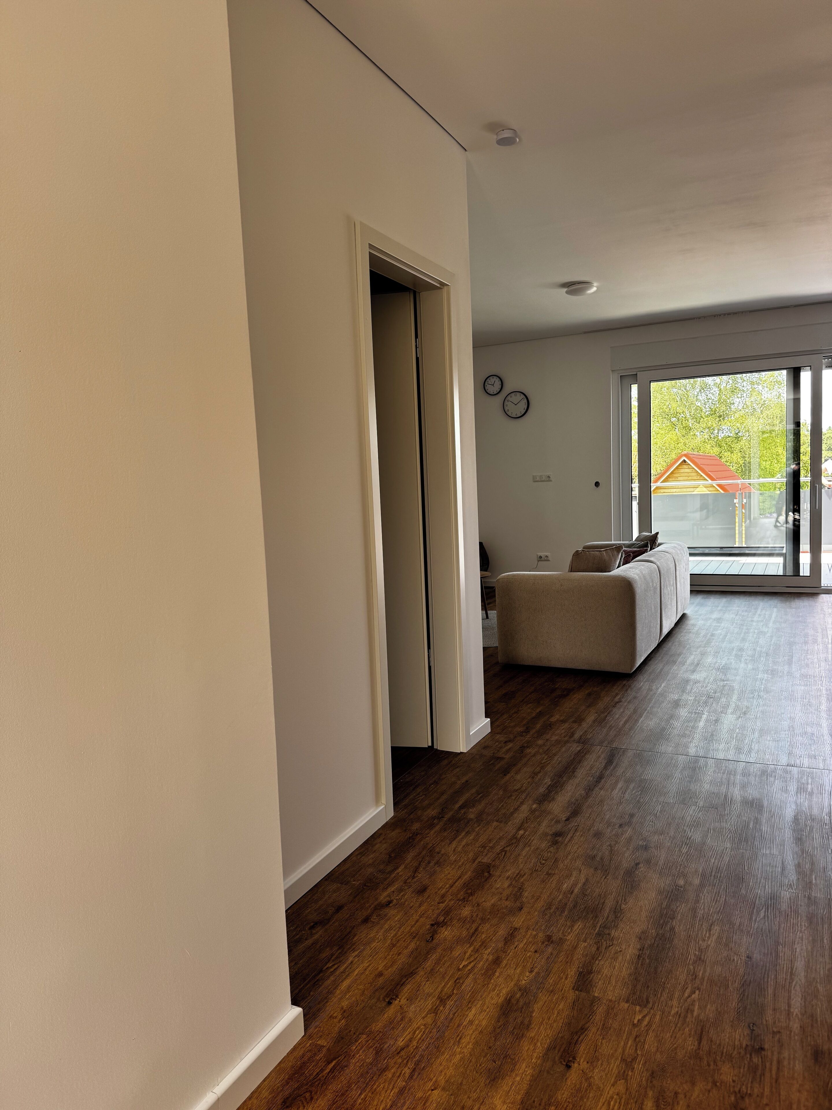 A spacious living room with a large window, a sofa, and a wooden floor.