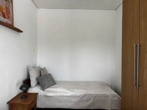 Et soveværelse med seng, puder, et natbord, en lampe og et klædeskab.