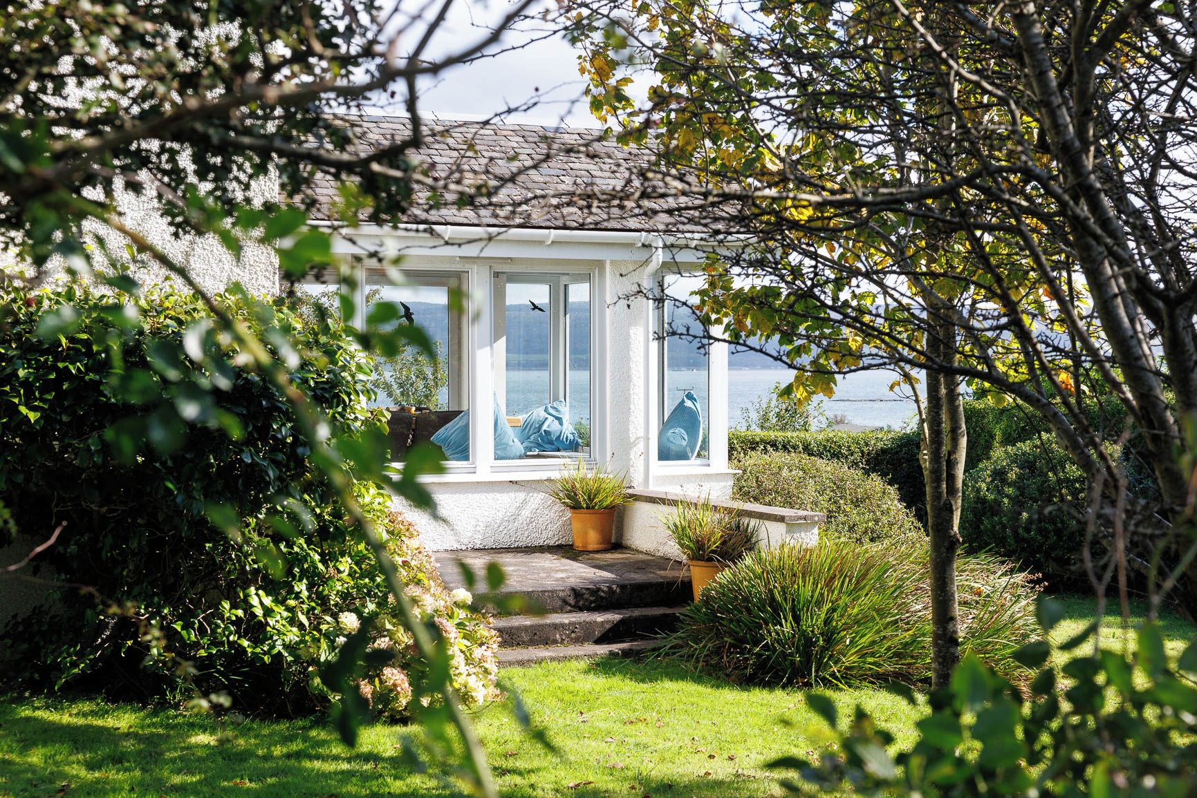 A conservatory with a view of the sea, surrounded by lush greenery.