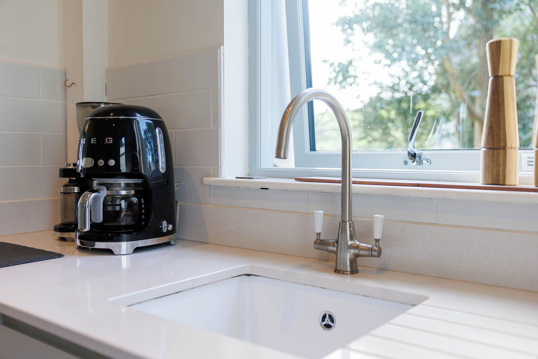 Een keuken met een koffiezetapparaat, een spoelbak en een raam met uitzicht op bomen.