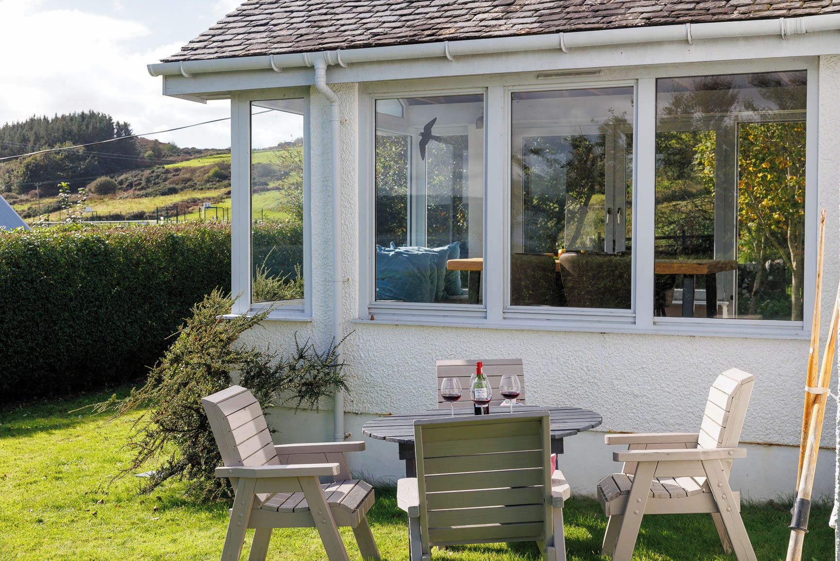 A covered patio with a table and chairs, a bottle of wine, and a bird on the window sill.