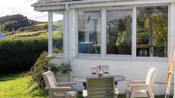 A covered patio with a table and chairs, a bottle of wine, and a bird on the window sill.