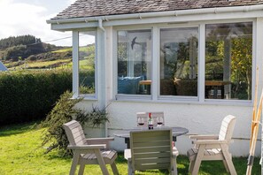 A covered patio with a table and chairs, a bottle of wine, and a bird on the window sill.