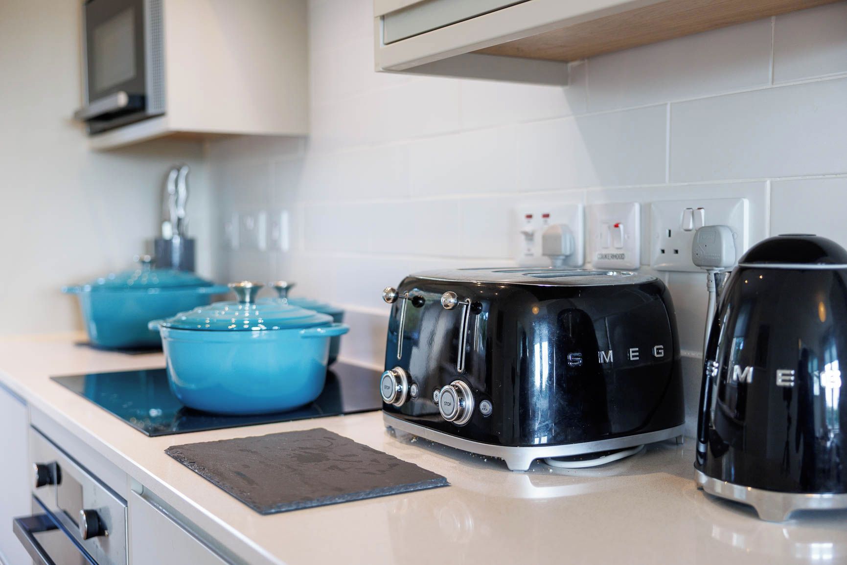 Een keuken met een zwarte broodrooster, blauwe pannen en een waterkoker.