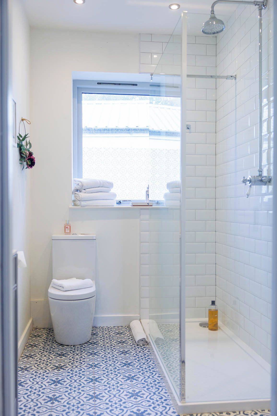 A bathroom with a white toilet, a glass shower enclosure, a patterned floor, and a window with a view.