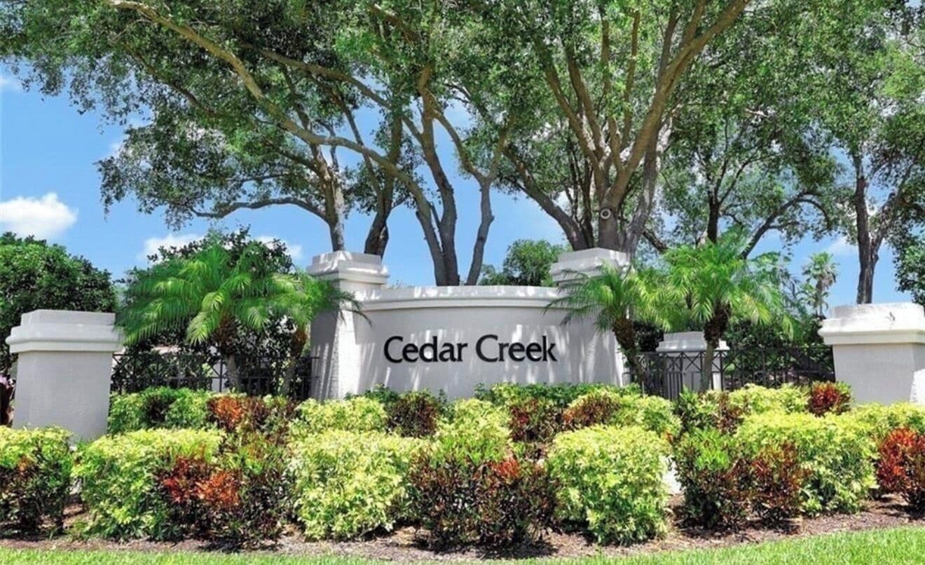 A sign with 'Cedar Creek' written on it, surrounded by lush greenery and trees.