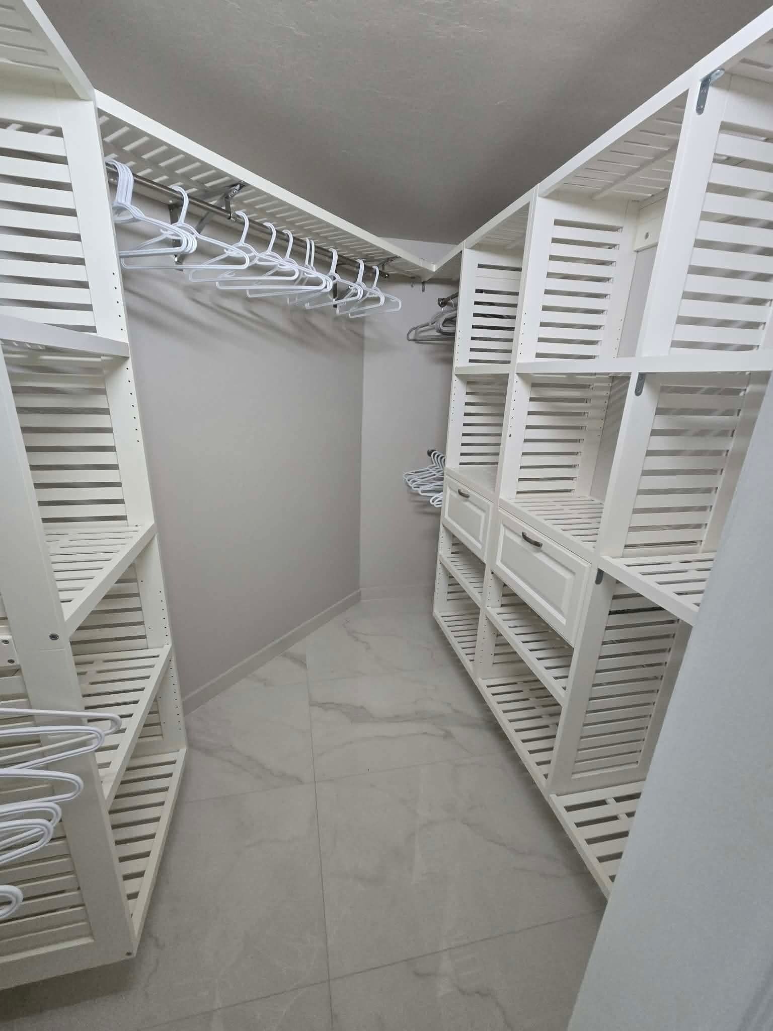 Un dressing avec des étagères blanches et une tringle pour suspendre les vêtements.