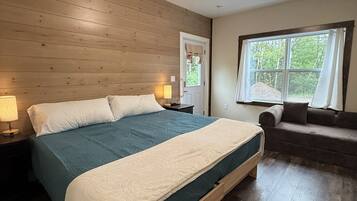 Een slaapkamer met een houten bed, een nachtkastje, een raam met gordijnen en een bank.