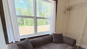 A room with a large window, a grey sofa, and a white radiator. - Sakura Valley Studio Suite #10 / Private Entrance in beautiful Annapolis Valley (North Alton)