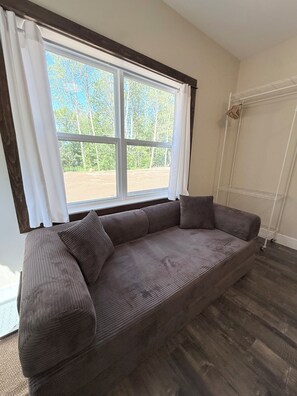 A room with a large window, a grey sofa, and a white radiator. - Sakura Valley Studio Suite #10 / Private Entrance in beautiful Annapolis Valley (North Alton)