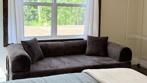 A bedroom with a bed, a dark brown sofa, a window with curtains, and a white wall. - Sakura Valley Studio Suite #10 / Private Entrance in beautiful Annapolis Valley (North Alton)
