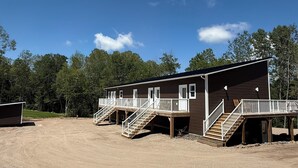 A row of wooden cabins with external staircases, set against a backdrop of trees and a clear sky. - Sakura Valley Studio Suite #10 / Private Entrance in beautiful Annapolis Valley (North Alton)