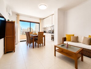 A modern living room with a dining area, a sofa, and a kitchen in the background. - Apartment Rocha | Sea View & Pool | Pulse (Praia da Rocha)