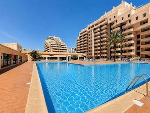 A swimming pool with lounge chairs, a lifebuoy, and a building with multiple balconies. - Apartment Rocha | Sea View & Pool | Pulse (Praia da Rocha)