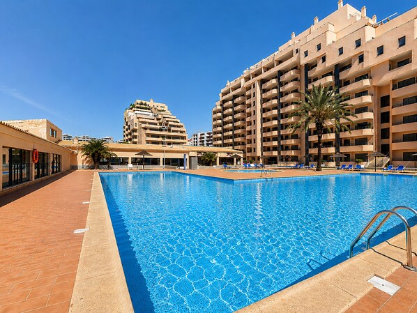 A swimming pool with lounge chairs, a lifebuoy, and a building with multiple balconies. - Apartment Rocha | Sea View & Pool | Pulse (Praia da Rocha)