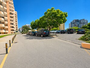 A parking lot with multiple cars, a tree, and buildings in the background. - Apartment Rocha | Sea View & Pool | Pulse (Praia da Rocha)