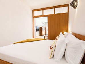 A hotel room with a bed, wooden headboard, and a view of a hallway with a wardrobe and a television. - Apartment Rocha | Sea View & Pool | Pulse (Praia da Rocha)