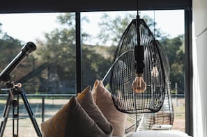 A room with a telescope, a hanging light fixture, and a view of trees through large windows. - Villa Boutique(+12) Alberca privada Valle de Gpe (San antonio de las minas)