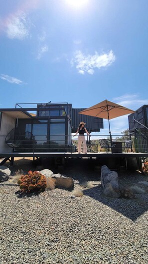 A person standing on a deck with a large umbrella, overlooking a modern building with a glass facade. - Villa Boutique(+12) Alberca privada Valle de Gpe (San antonio de las minas)