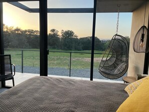 A bedroom with a large window, a hanging chair, and a bed with a patterned bedspread. - Villa Boutique(+12) Alberca privada Valle de Gpe (San antonio de las minas)