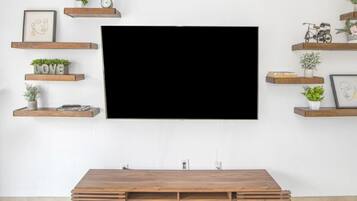 A flat-screen TV mounted on a white wall with wooden shelves above and below it, holding decorative items and plants.