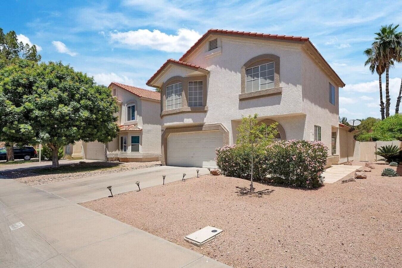 A two-story house with a garage, a driveway, and a landscaped front yard with a small tree and shrubs.