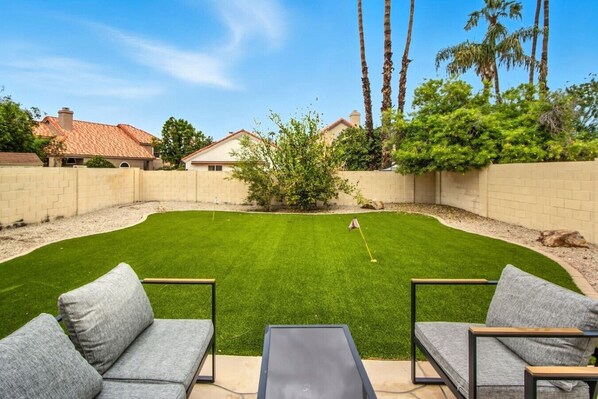 A backyard with a lawn, a putting green, and a patio area with seating. - Casa de Arizona: 3 BR Luxury Stay + King Bed (Gilbert)