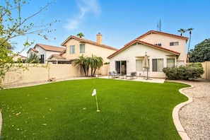 A residential property with a well-maintained lawn, patio furniture, and a flag indicating a golf course. - Casa de Arizona: 3 BR Luxury Stay + King Bed (Gilbert)
