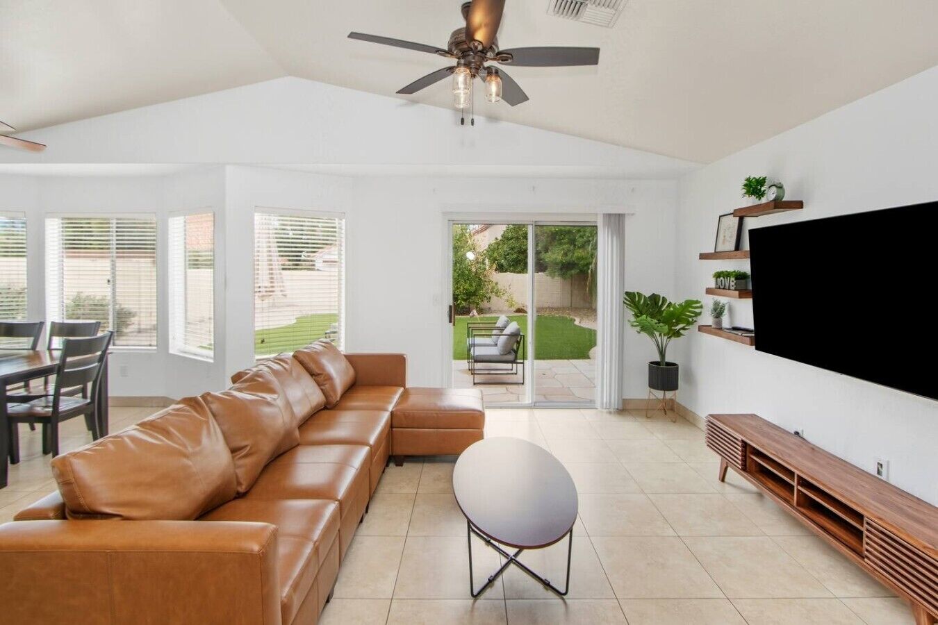 A spacious living room with a leather sofa, a round table, and a flat-screen TV mounted on the wall.