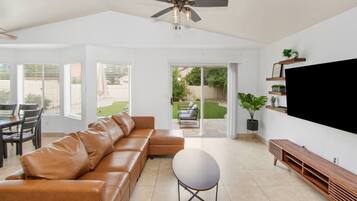 A spacious living room with a leather sofa, a round table, and a flat-screen TV mounted on the wall.