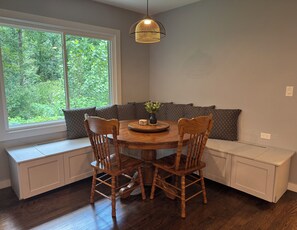 Un coin repas comprenant une table ronde en bois, quatre chaises, un banc avec des coussins et un luminaire suspendu.