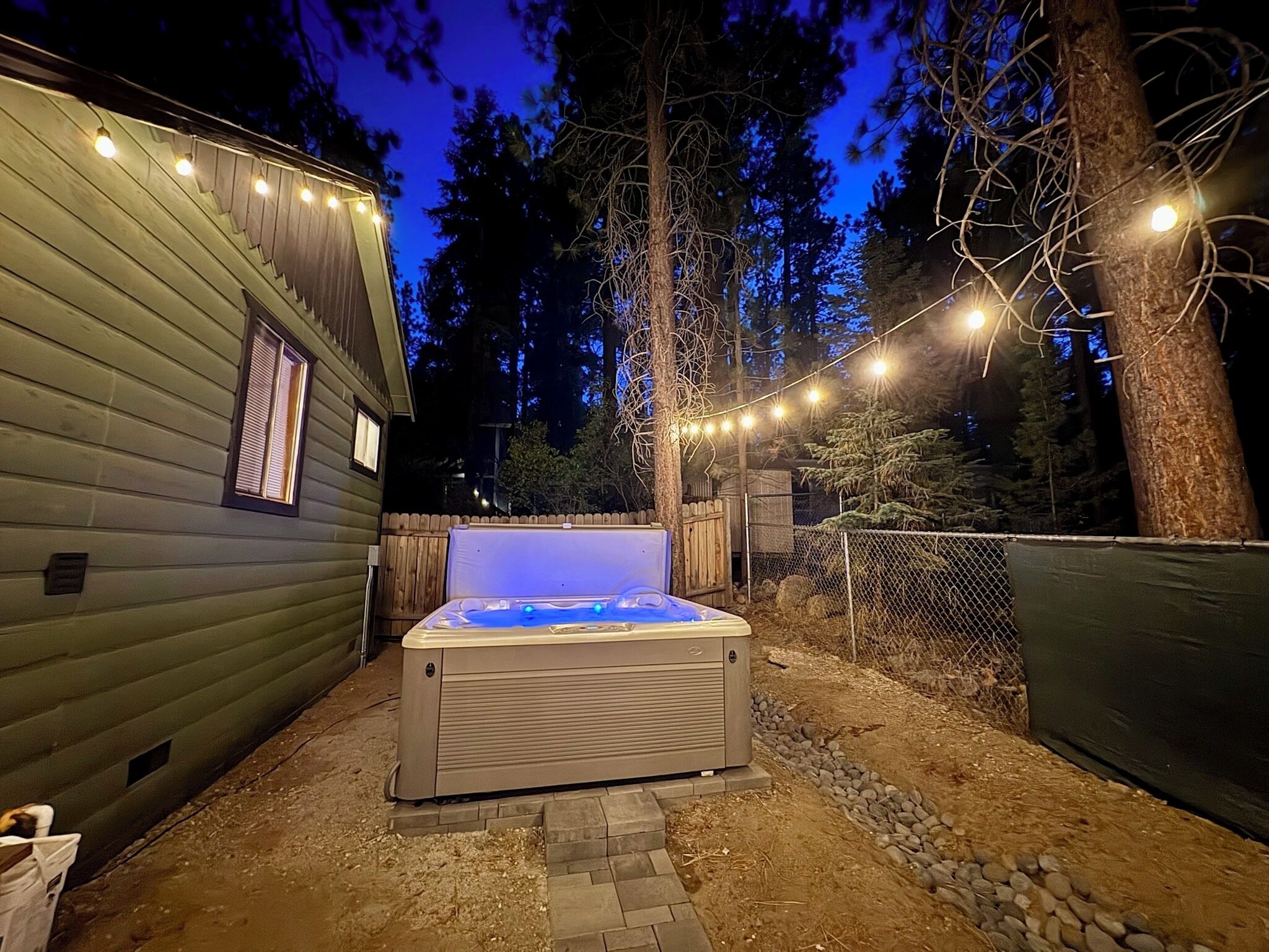 A hot tub in a backyard with a wooden deck and string lights.