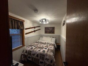 Een slaapkamer met een bed, een raam met zonwering, een wandlamp en een lijst met een afbeelding.