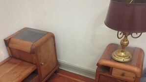 Una habitació d'angle amb una arca de prestatges de fusta, una taula petita amb una làmpada i un sòl de fusta amb dibuixos.