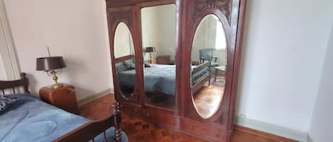 A bedroom with a wooden bed, a wooden dresser with mirrors, a nightstand with a lamp, and a wooden floor.