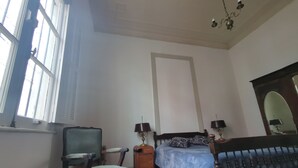 Una habitació amb un llit, una cadira, una taula, una làmpada i un mirall.
